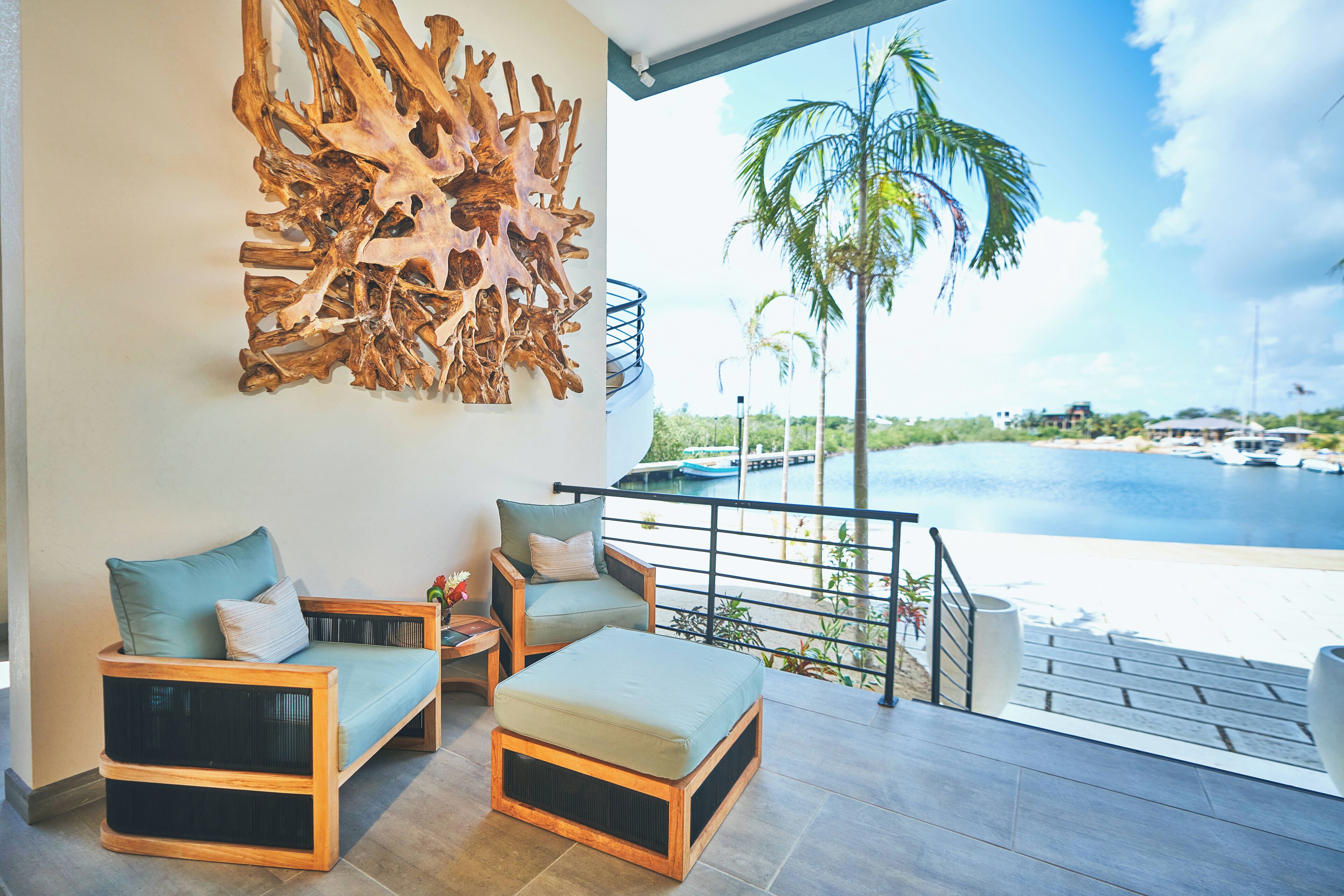 Ein Balkon mit Blick auf das Wasser, eine Holzskulptur an der Wand und zwei Stühle mit Kissen.