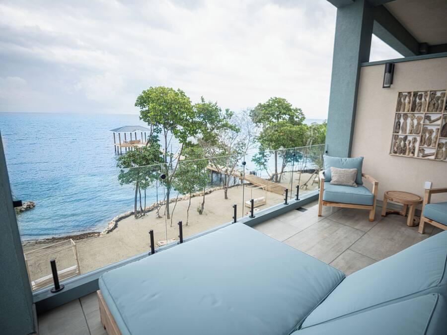 Un balcón con vista al mar, una terraza de madera y una zona de estar con cojines.