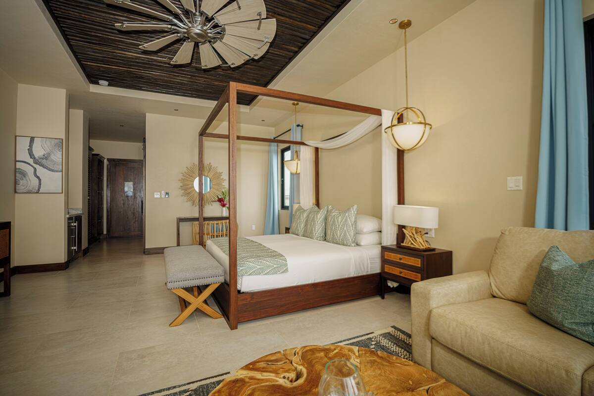 A spacious bedroom with a four-poster bed, a sitting area with a sofa, and a dining table.