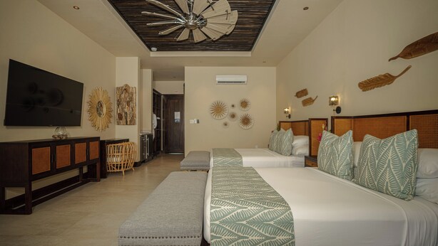 A hotel room with two beds, a large flat-screen TV, a ceiling fan, and decorative wall art. - Prana Maya Island Resort (Placencia)
