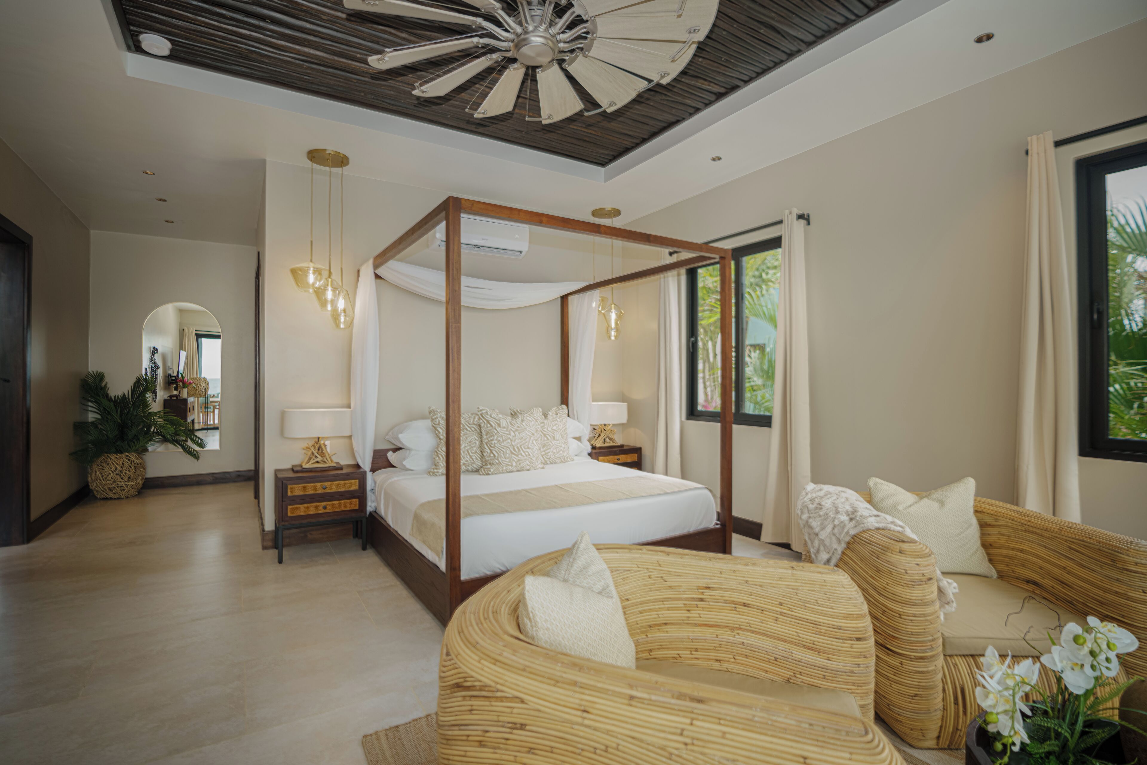 A spacious bedroom with a four-poster bed, a sitting area with a sofa, and a large window offering a view of greenery.