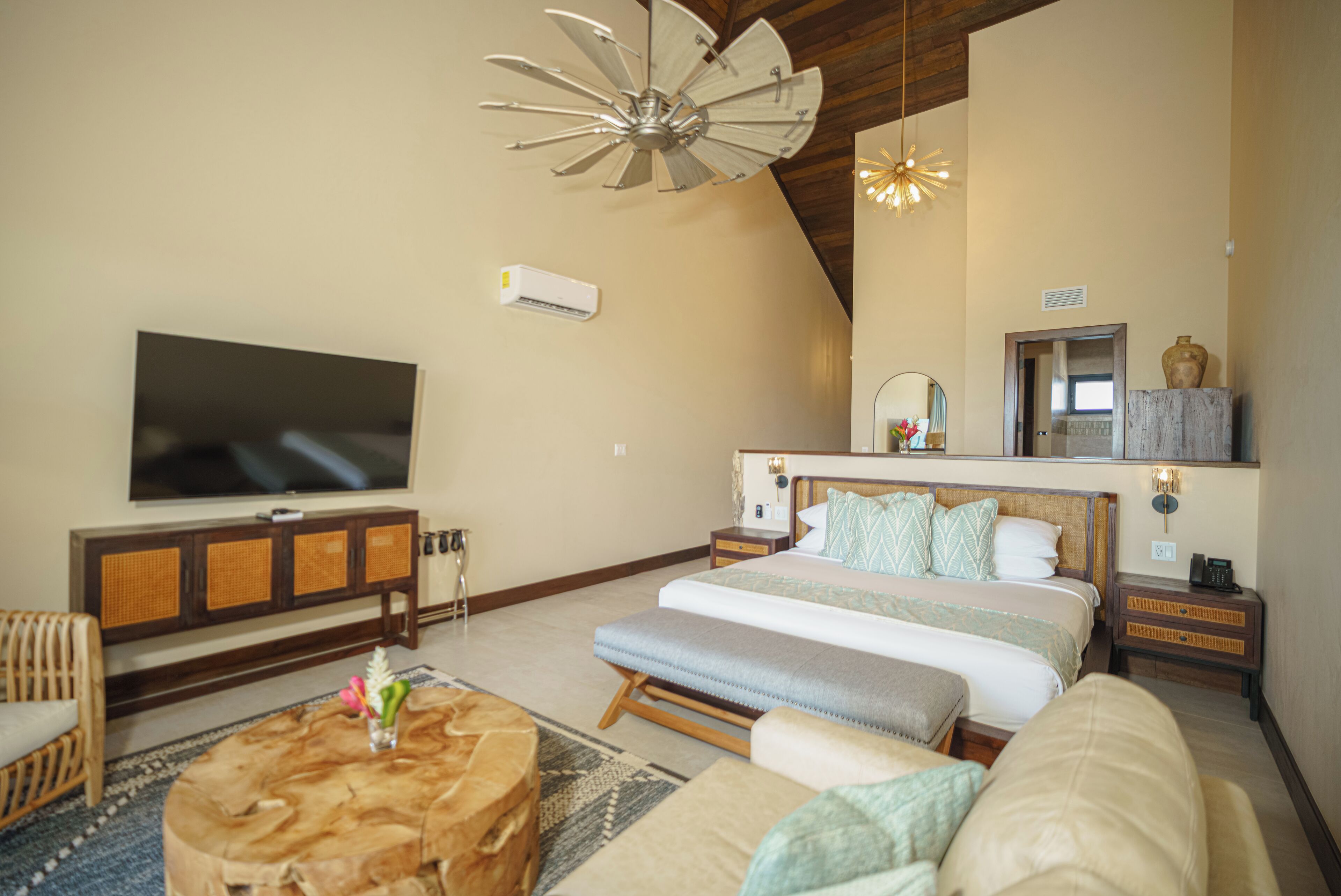 A spacious bedroom with a large bed, a flat-screen TV, a wooden headboard, and a ceiling fan.