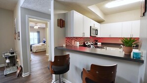 Cozinha moderna com armários brancos, bancada preta e backsplash vermelho. Há dois banquetes e uma planta em vasos sobre a bancada.
