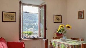 A room with a window overlooking a scenic view, a dining table with a colorful tablecloth, and a red sofa. - Mansion on Fishermen's Isle (Stresa)