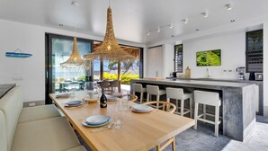 Une cuisine moderne dotée d’un îlot central, de tabourets de bar et d’un coin repas avec une table et des chaises en bois.