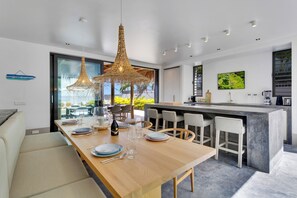 Een moderne keuken met een centraal eiland, barstoelen en een eethoek met een houten tafel en stoelen.