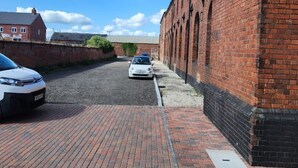 Une rue étroite, avec un bâtiment en briques d’un côté et une voiture garée de l’autre.