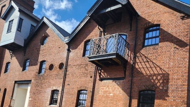 Un immeuble à plusieurs étages, construit en briques, avec un toit plat, un balcon doté d  ’une rambarde en métal et une porte de garage.