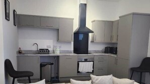 Une cuisine moderne avec des meubles gris, une hotte noire et un coin repas agrémenté d’une chaise noire.