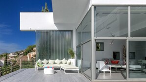 A modern outdoor living area with a sofa set, a coffee table, and a glass wall offering a view of a hillside. - Villa Petrer in Javea X bia (Javea)