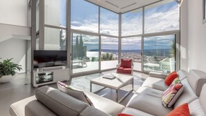 A modern living room with a large TV, comfortable seating, and a view of the city through large windows. - Villa Petrer in Javea X bia (Javea)