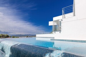 A modern infinity pool with clear blue water, a white building with a balcony, and a mountainous landscape in the background. - Villa Petrer in Javea X bia (Javea)