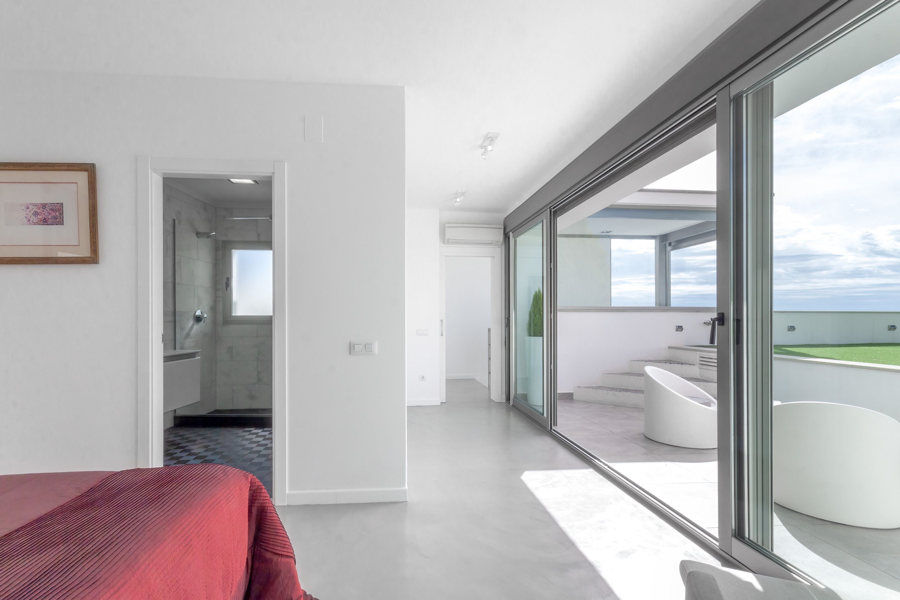Ein modernes Hotelzimmer mit einer großen Schiebeglastür, die auf einen Balkon mit Blick auf den Himmel und einen Pool führt.