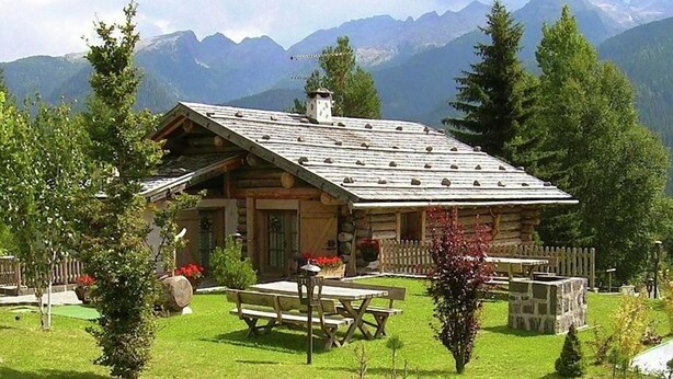 Une cabane en rondins avec un toit en pente, entourée d’un jardin bien entretenu, agrémenté d’une table de pique-nique et de bancs.