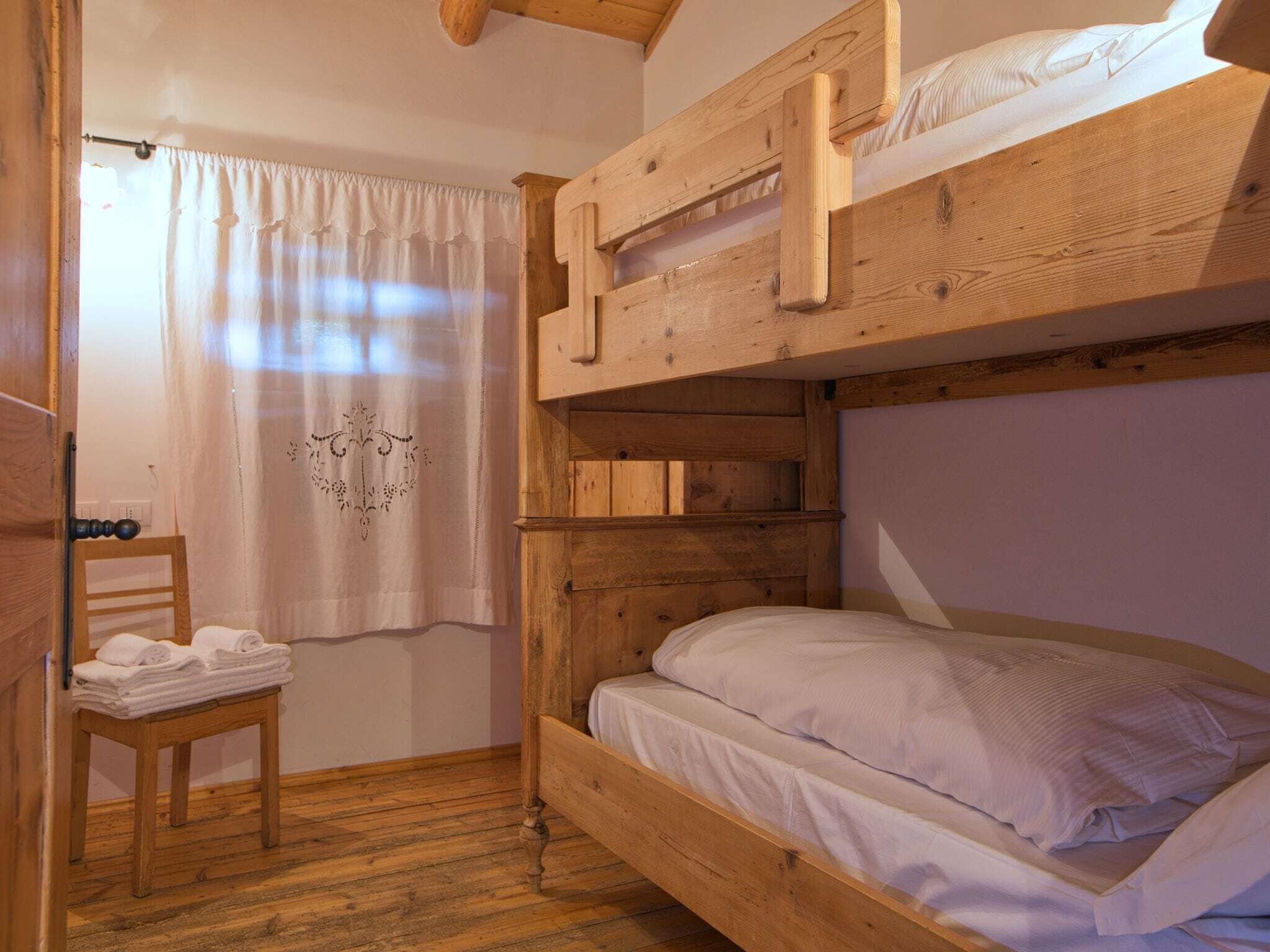 Une chambre avec un lit superposé, une chaise en bois et un rideau.