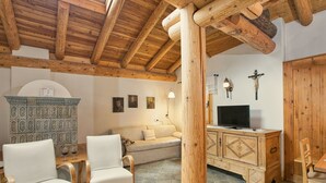 Un intérieur rustique avec des poutres en bois, un canapé, deux fauteuils, un buffet et un téléviseur.