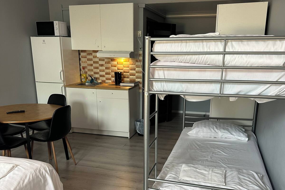 Quarto compacto com beliches, cozinha compacta, área de refeições e uma mesa pequena.