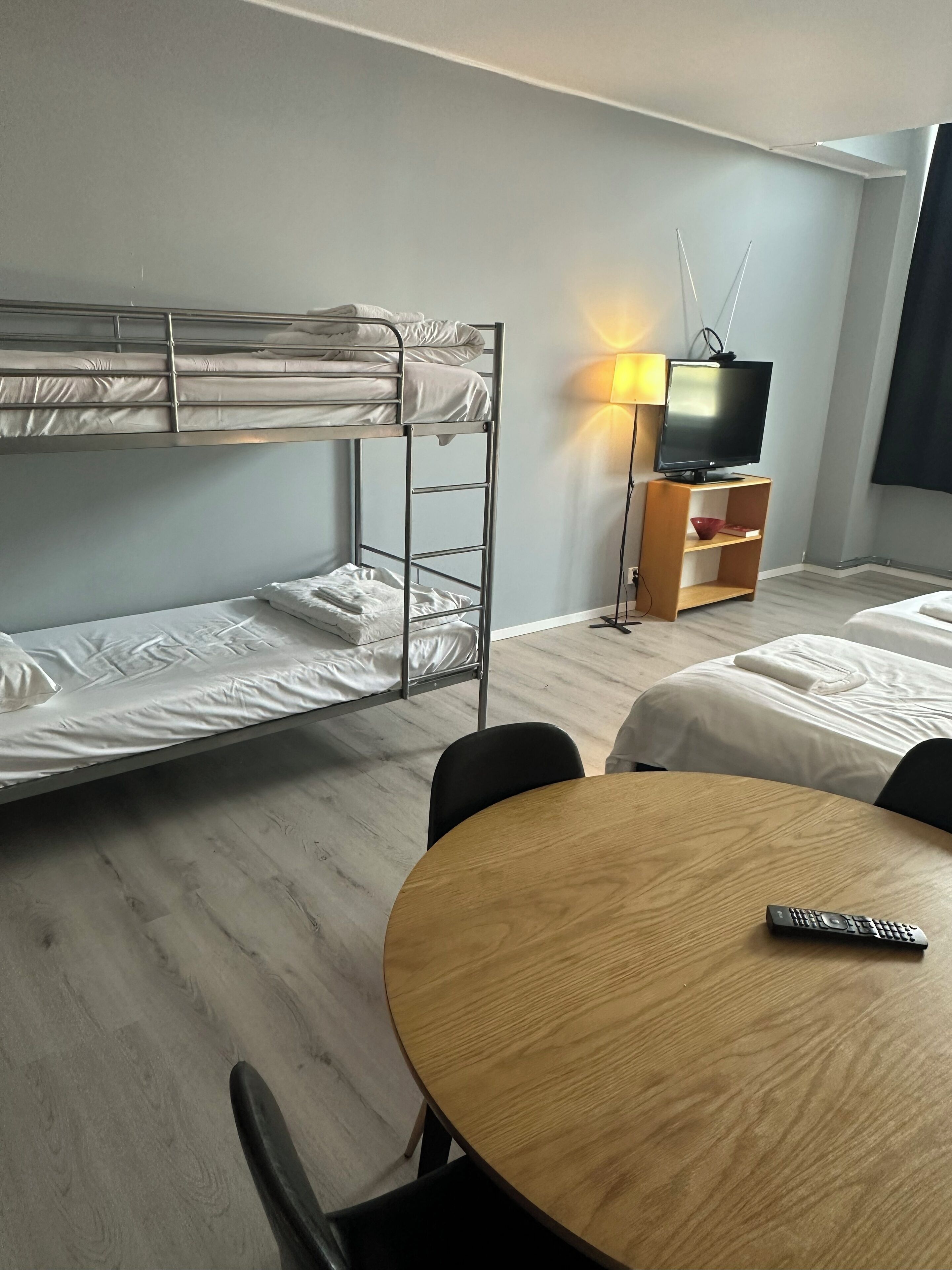 Een kamer met stapelbedden, een televisie, een lamp en een ronde houten tafel met een afstandsbediening.