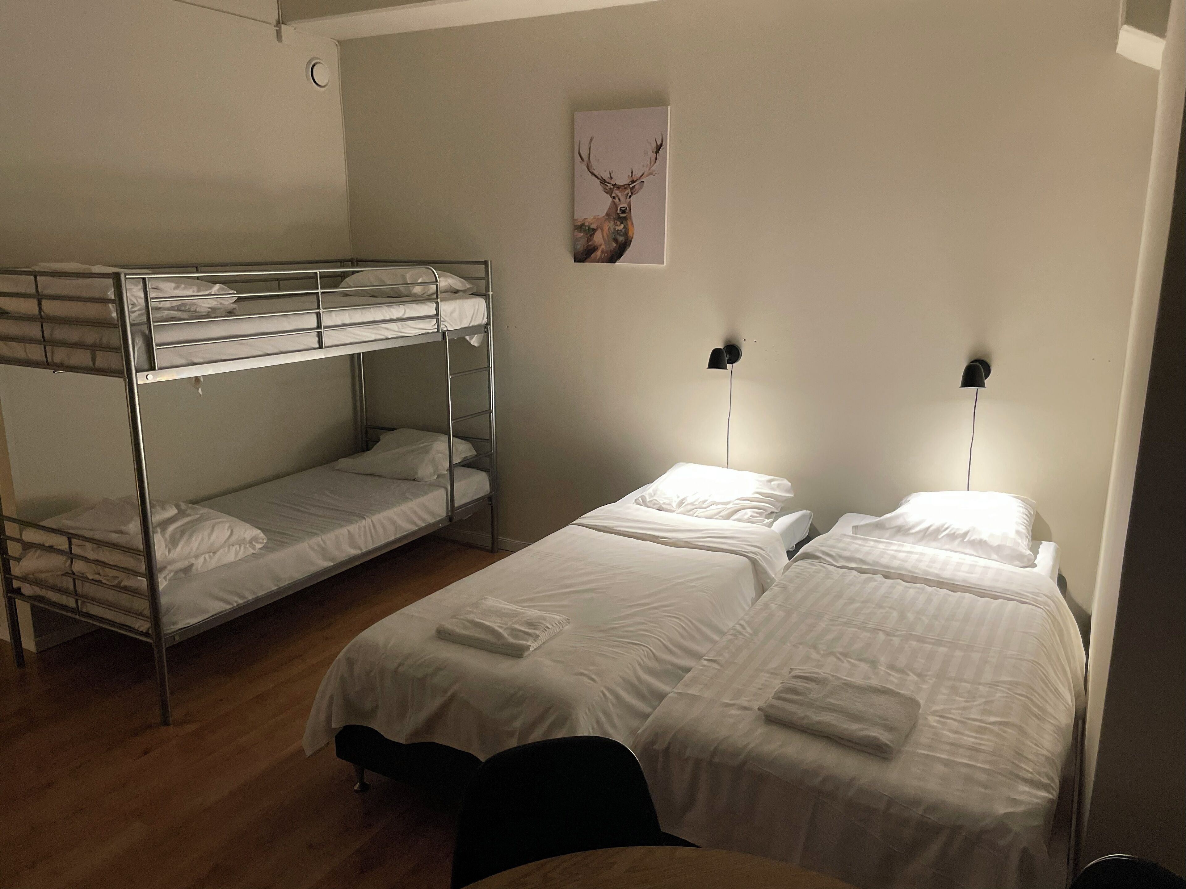 A dormitory room with bunk beds and two single beds, a wall-mounted light, and a framed picture.
