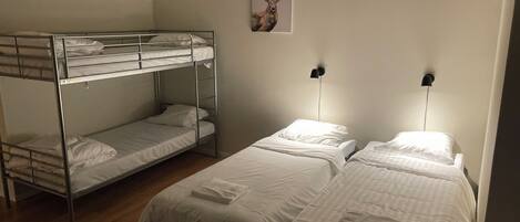 A dormitory room with bunk beds and two single beds, a wall-mounted light, and a framed picture.