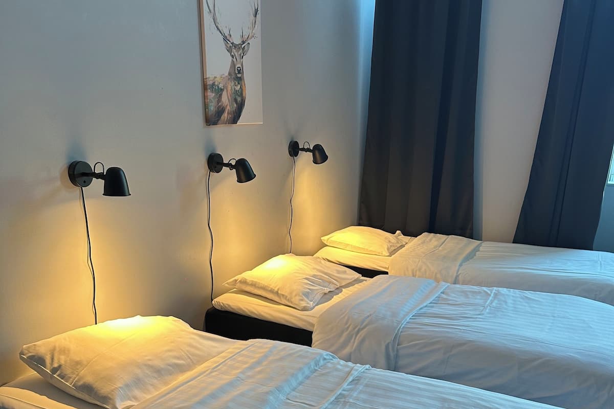 Quarto de hotel com duas camas de solteiro, cada uma com roupa de cama branca e luminária na cabeceira.