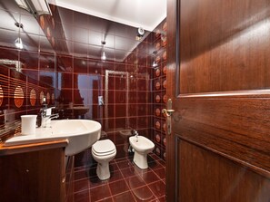 Un baño con un lavamanos blanco, un inodoro y un bidé. Las paredes están cubiertas de baldosas rojas brillantes.