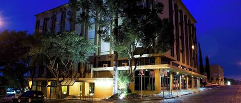 Un hotel de varios pisos con entrada a nivel de calle, ventanas amplias y una calle pavimentada frente al edificio.