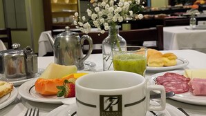 A breakfast setting with plates of food, a coffee cup, and a vase with flowers. - Planalto Hotel (Canoinhas)