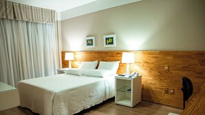A hotel room with a wooden headboard, a bed with white linens, two bedside lamps, and a nightstand with a lamp and phone. - Planalto Hotel (Canoinhas)
