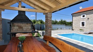 Une terrasse extérieure avec un barbecue en pierre, une table en bois, une lanterne et une piscine.