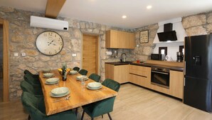 Une cuisine moderne avec des murs en pierre, des meubles en bois, une table à manger avec des chaises et un réfrigérateur noir.