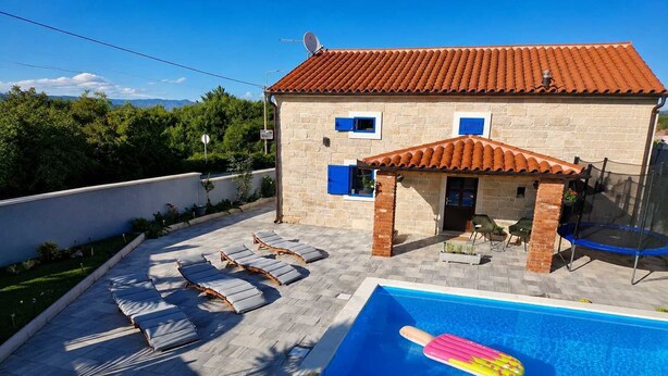 Un bâtiment en pierre avec un toit en tuiles, une piscine et des chaises longues.