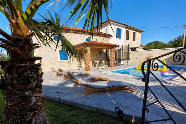 A villa with a swimming pool, sun loungers, and a palm tree.