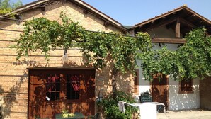 Un bâtiment rustique avec une façade en briques, une porte en bois et une table entourée de chaises à l’extérieur.