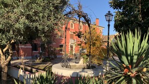 Un patio con una fuente, rodeado de árboles y un edificio de paredes rojas.