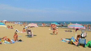 Una playa concurrida con gente tomando el sol y paseando.