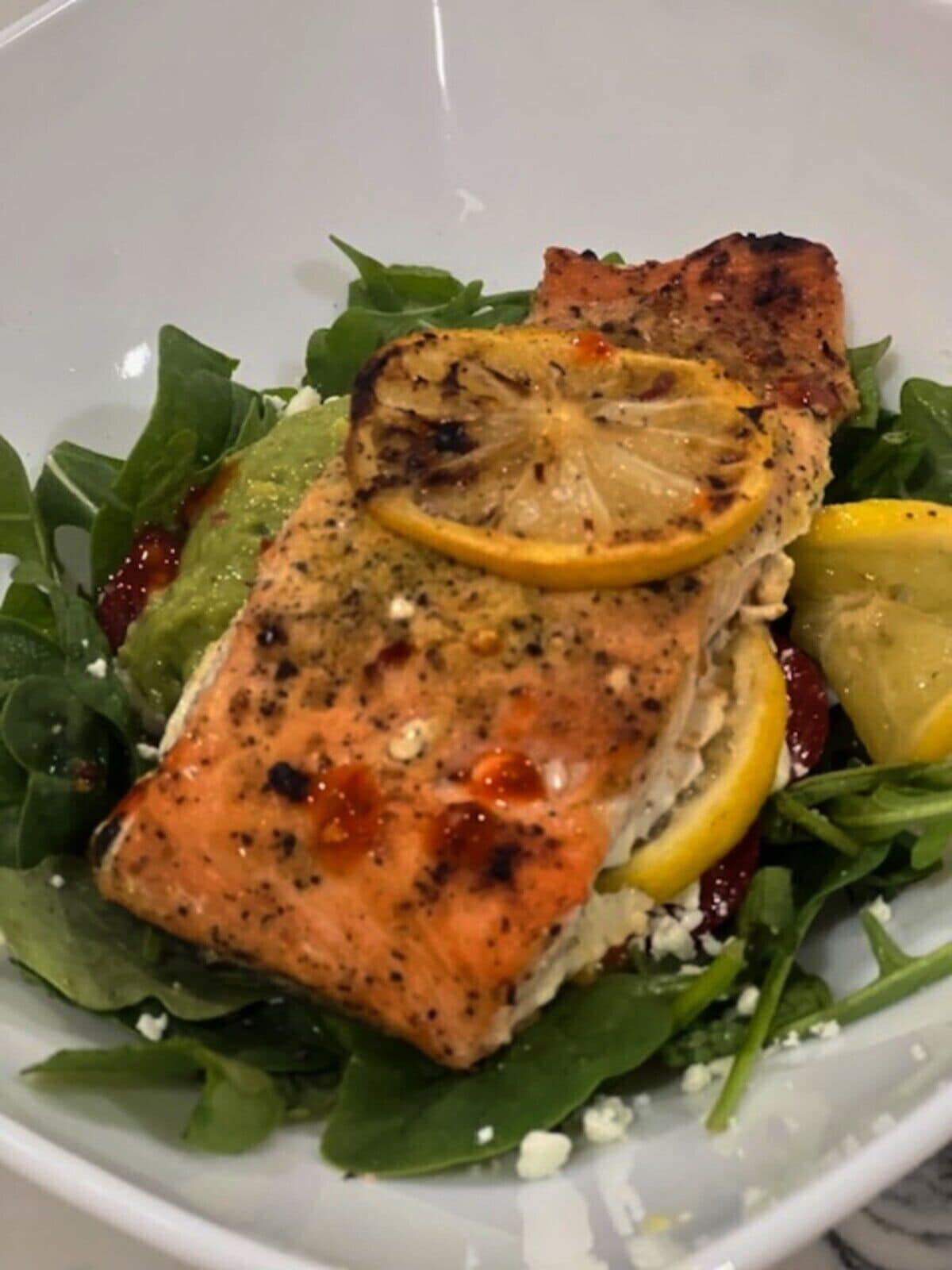 A plate with grilled salmon, lemon slices, and a salad.
