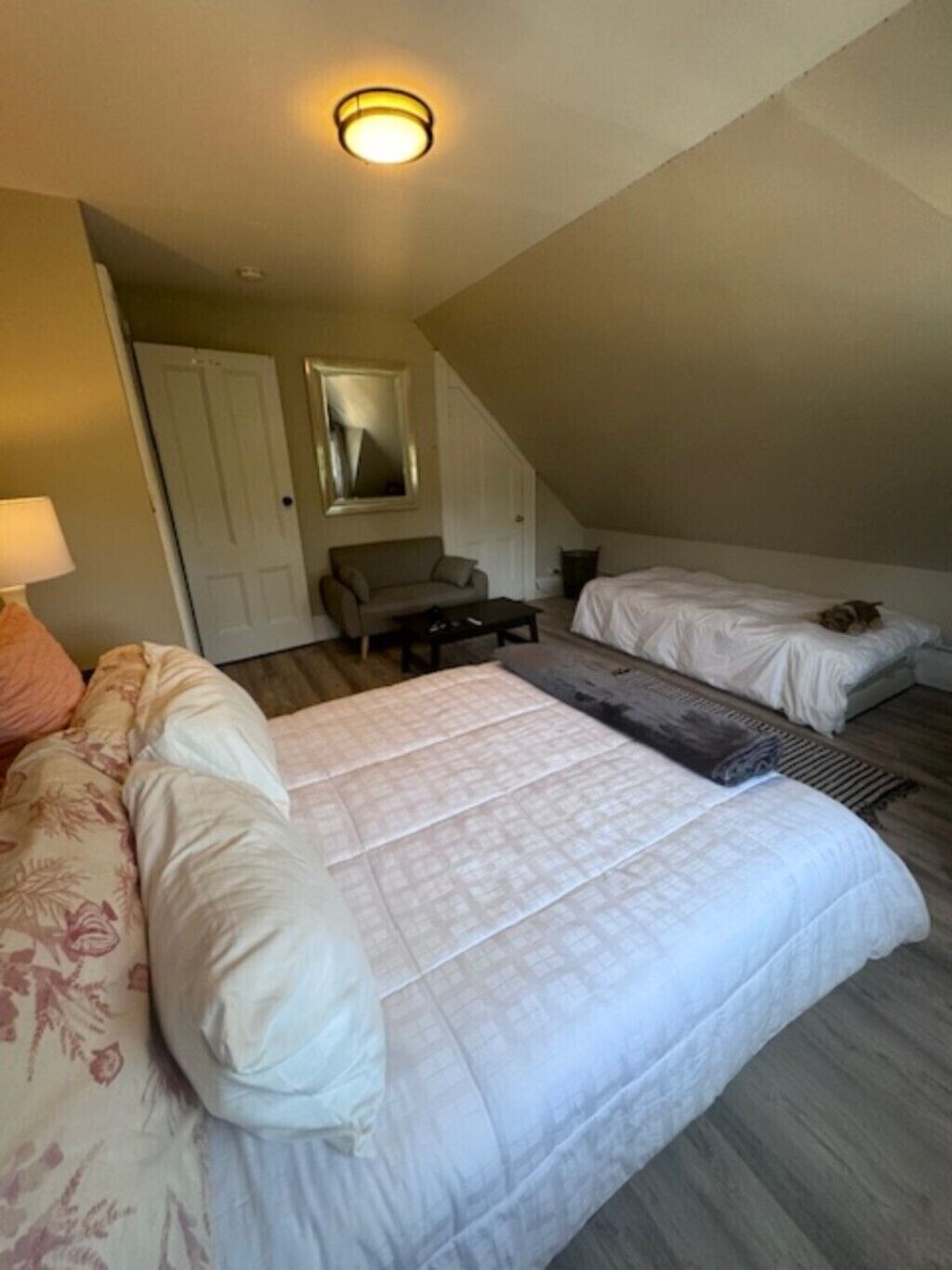 A bedroom with a large bed, a smaller bed, a sofa, a coffee table, and a mirror.