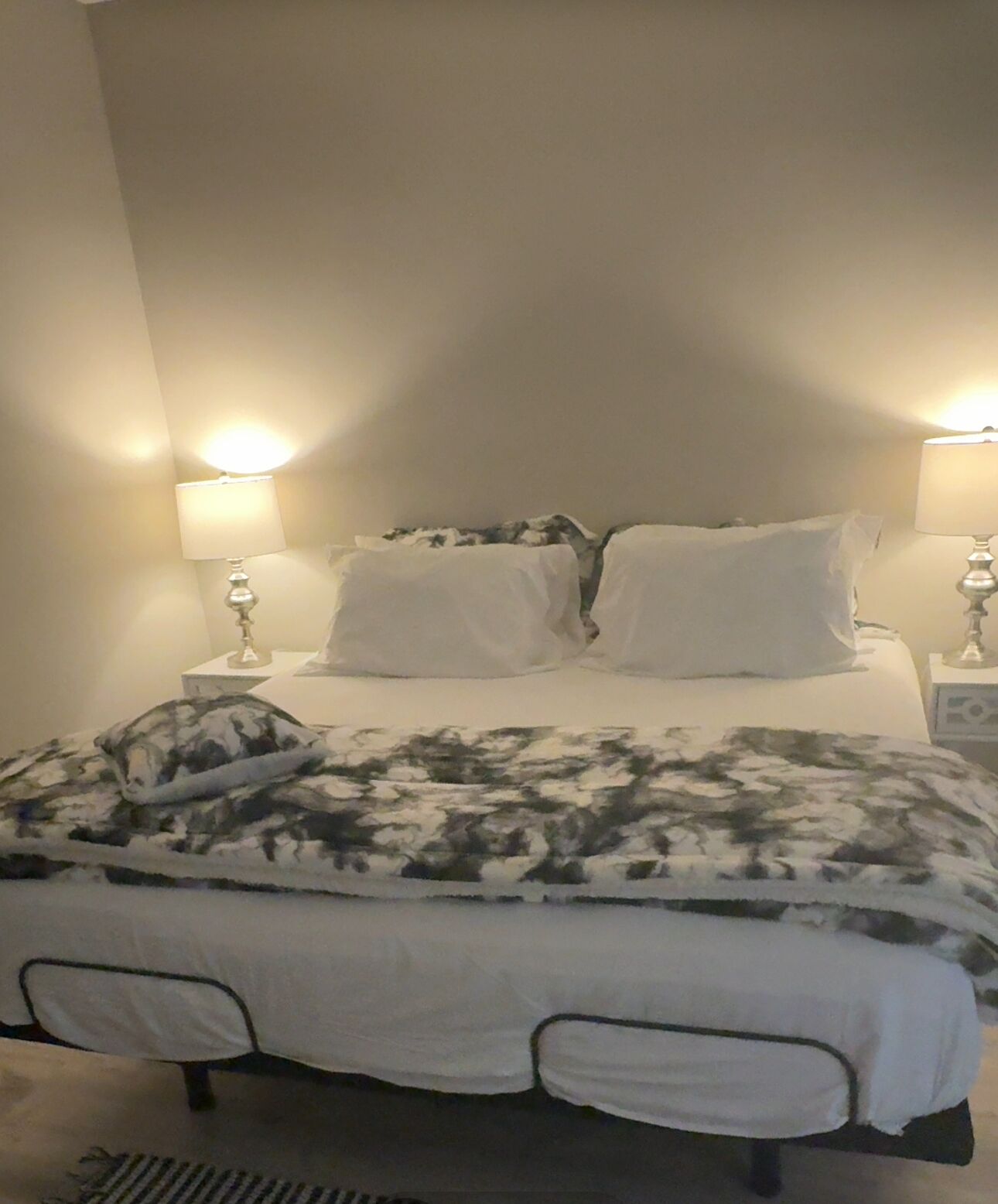 A bed with white bedding and a camouflage-patterned blanket, two bedside lamps, and a plain wall.