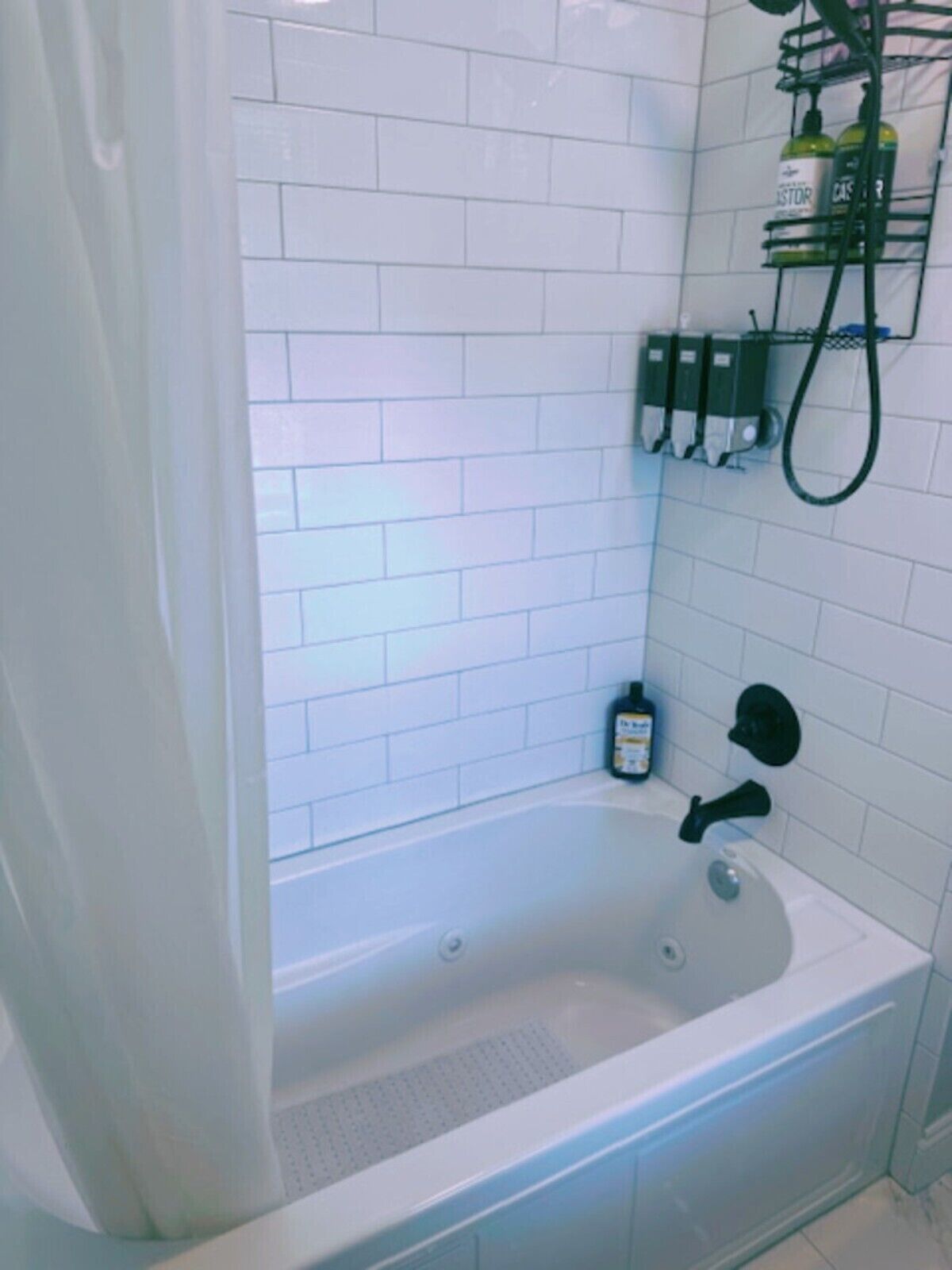 A bathroom with white tiled walls, a bathtub, a shower head, and a shelf with toiletries.