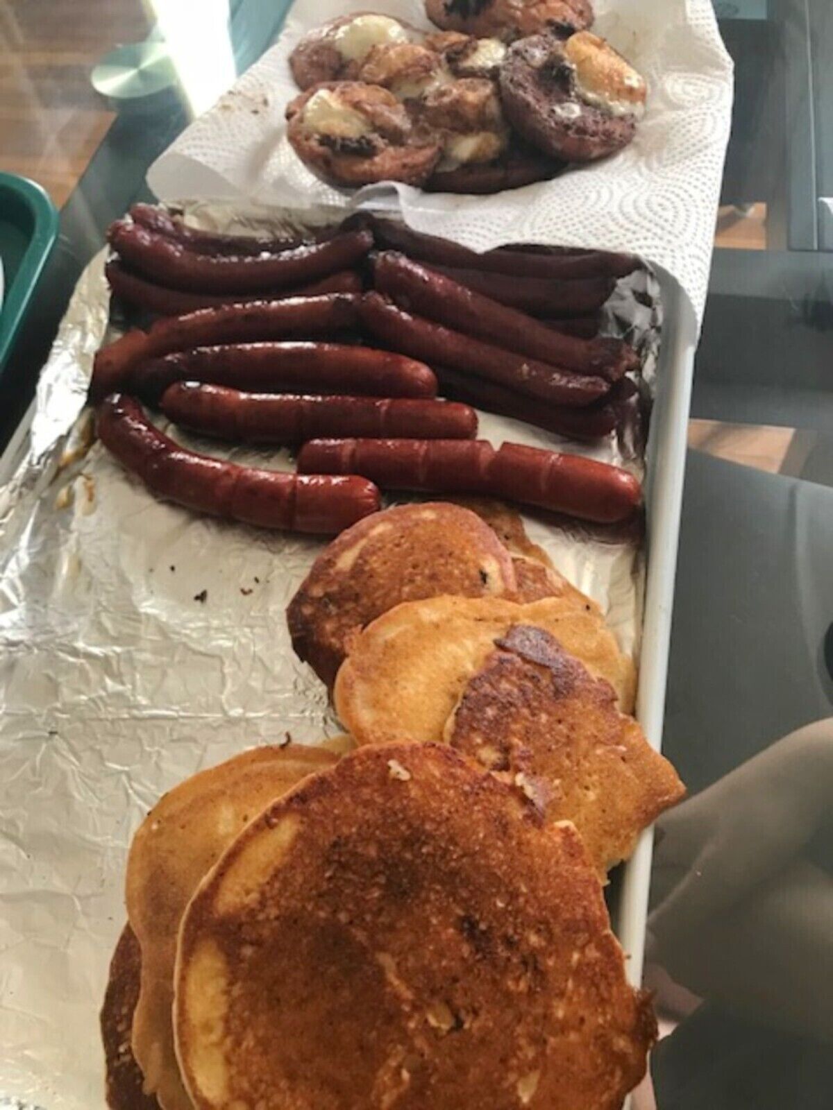 A tray with sausages, pancakes, and a piece of bread on a foil-lined surface.