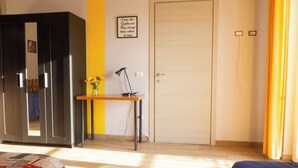 A bedroom with a bed, a desk with a lamp, a wardrobe, and a door.