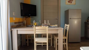 A kitchen with a dining table, chairs, a television mounted on the wall, a refrigerator, and a door.