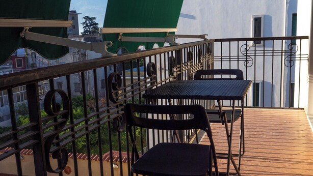 A balcony with a table and chairs, a green awning, and a view of buildings and mountains.