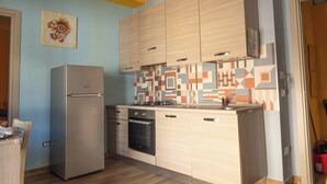 A compact kitchen with light wood cabinets, a stainless steel refrigerator, and a patterned backsplash.