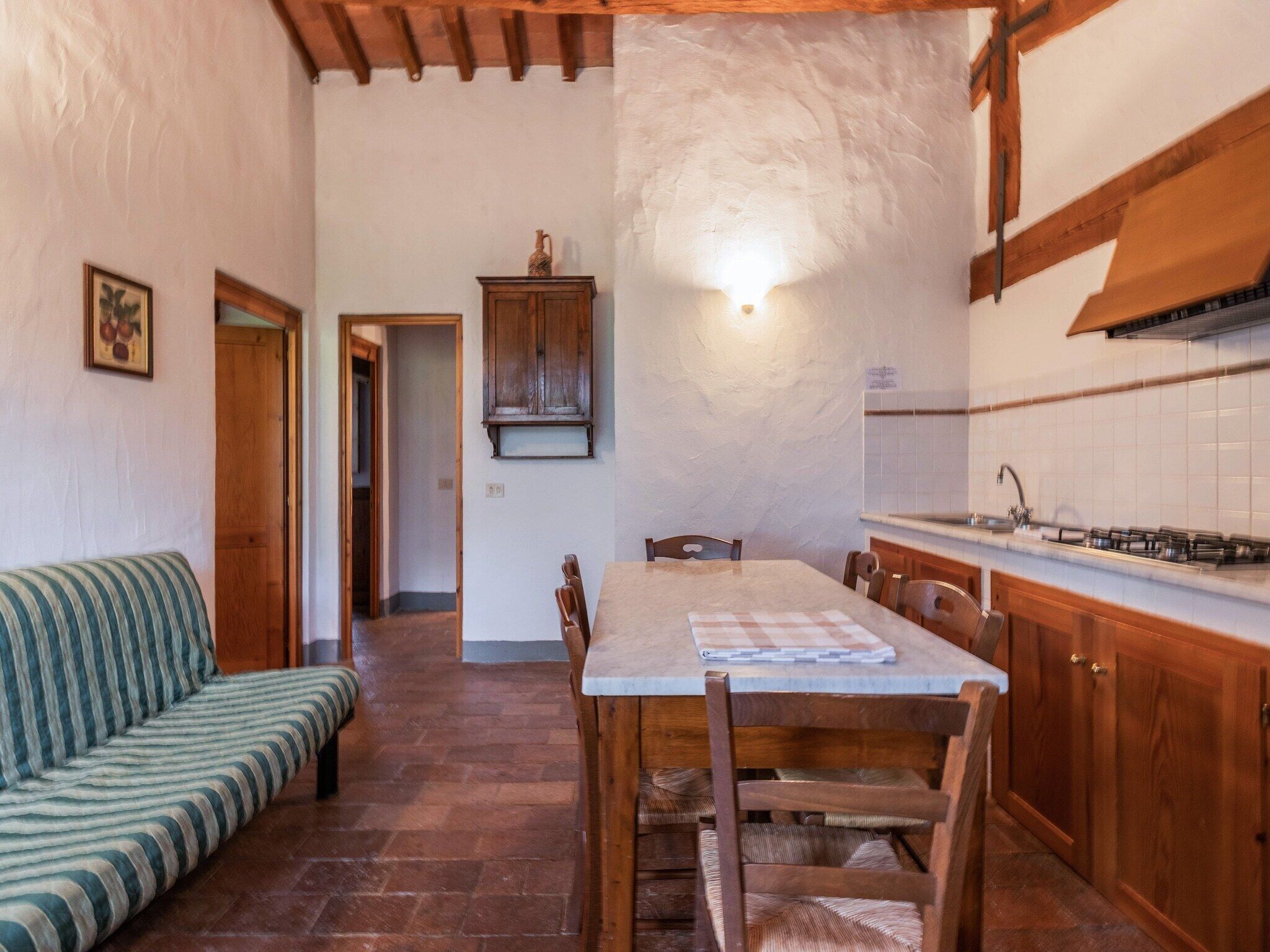 Une cuisine chaleureuse avec une table à manger, des chaises en bois, un canapé à rayures et un mur recouvert de carreaux.