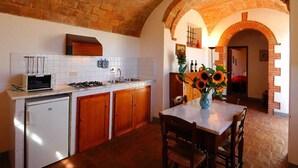 A kitchen with a brick archway, white tiled backsplash, wooden cabinets, a built-in oven, and a dining area with a table and chairs.