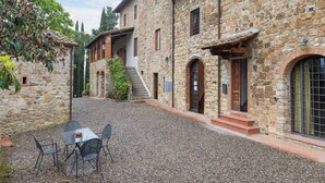 A stone building with a gravel courtyard, outdoor seating, and a staircase leading to the entrance.