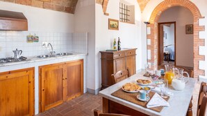 A kitchen with a brick archway, white tiled backsplash, wooden cabinets, and a dining area with breakfast items.