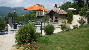 Un restaurante con terraza, horno de piedra y vistas a las montañas.